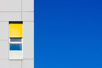 Modern minimalist building facade with vibrant yellow window against a clear blue sky, showcasing contemporary design. HD wallpaper
