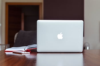 A clean and modern workspace featuring a laptop, book, and smart on a wooden table. HD wallpaper