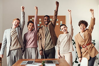 A diverse team celebrating success with raised hands in a modern office setting. HD wallpaper