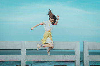 Woman jumping cheerfully on a bridge under a sunny blue sky, embodying dom and happiness. HD wallpaper