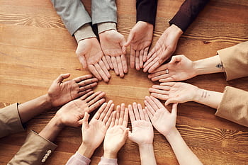 Top view of diverse hands forming a circle on a wooden table, symbolizing unity and diversity. HD wallpaper