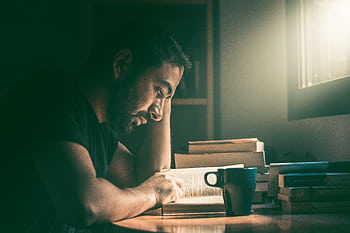 An adult man immersed in reading by the window in Madrid. Warm, focused study atmosphere. HD wallpaper