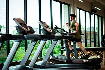 Young man workouts on treadmill in modern gym with large windows and natural light. HD wallpaper