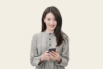 Smiling woman with long hair using her smart, wearing a casual outfit against a simple background. HD wallpaper