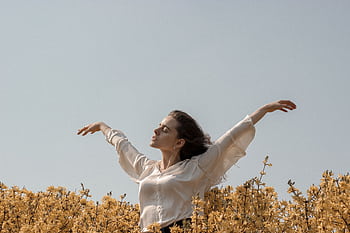 Woman with arms raised in a sunny field of yellow flowers, capturing dom and serenity. HD wallpaper
