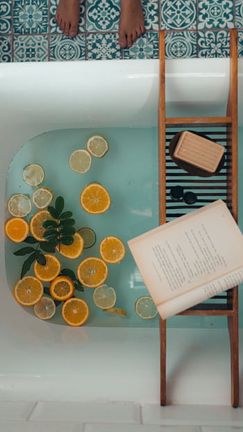 A serene bath setup with citrus fruits, a book, and a bar of soap for ultimate relaxation. HD phone wallpaper