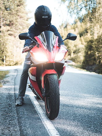 A motorcyclist wearing a helmet rides a red sports bike on a scenic forest road. HD phone wallpaper