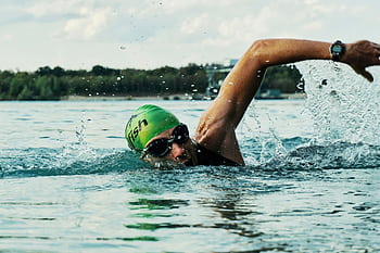 A male swimmer in a green cap and goggles competing in an open water race. HD wallpaper