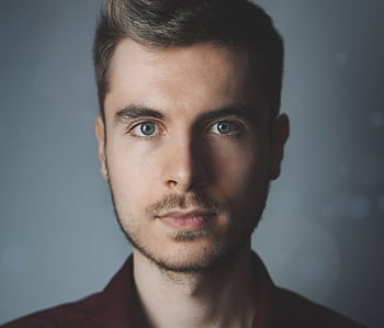 Close-up portrait of a young man with facial hair and a serious expression. HD wallpaper