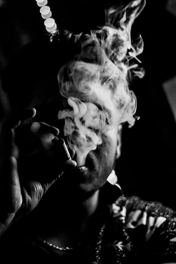 Man smoking with smoke obscuring face, captured in dramatic black and white. HD phone wallpaper