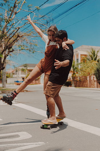 Happy couple experiencing joy and leisure while skateboarding together outdoors in Rio de Janeiro. HD phone wallpaper