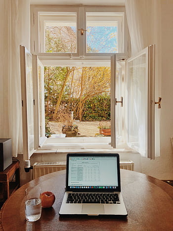 Cozy home office setup with laptop on desk facing an open window offering a view of a garden. HD phone wallpaper