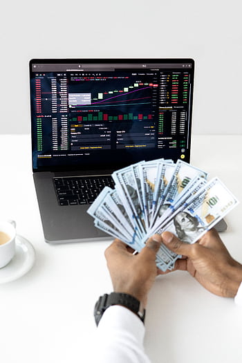 Hands holding cash in front of a laptop displaying stock market data, symbolizing financial growth and investment. HD phone wallpaper
