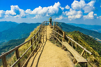 Hiker stands on a que trail in Thailand, surrounded by lush mountains and clouds. HD wallpaper