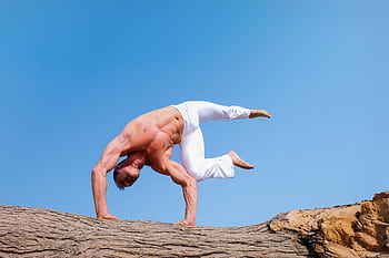 A man performs a dramatic handstand on rocks with a clear blue sky backdrop, showcasing fitness and balance. HD wallpaper
