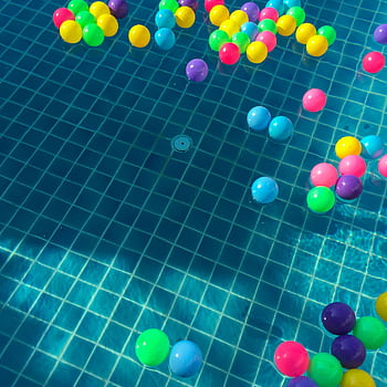 Floating colorful plastic balls in a sunlit swimming pool, creating a vibrant and playful scene. HD phone wallpaper