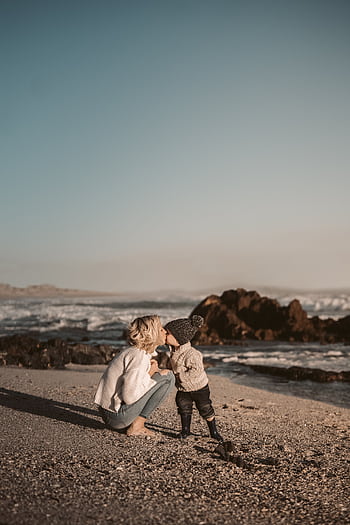 A touching scene of a mother and child sharing a kiss on a scenic beach during sunset. HD phone wallpaper