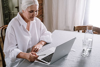 Elderly woman using laptop for online shopping at home during daytime. HD wallpaper