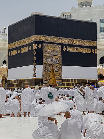 Pilgrims in white garments gather around the Kaaba in Mecca during daytime prayers. HD phone wallpaper