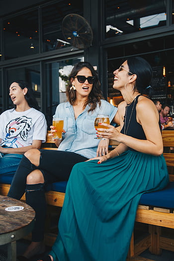 Three friends enjoying drinks and conversation at an outdoor bar. HD phone wallpaper