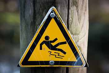 Close-up of a triangular warning sign indicating a slippery surface, fixed to a wooden post. HD wallpaper
