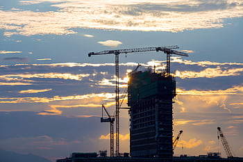 Silhouette of cranes and a building under construction against a vivid sunset sky. HD wallpaper