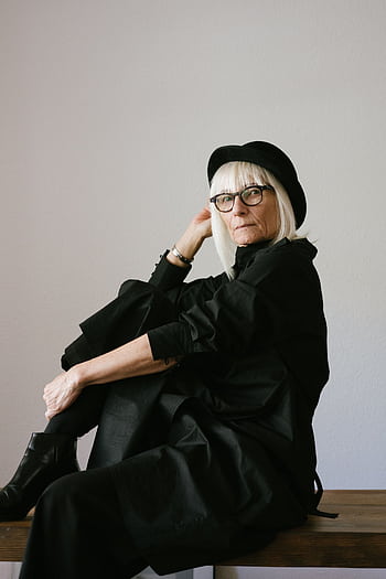 Elegant senior woman wearing eyeglasses and a black outfit posing indoors, showcasing timeless fashion. HD phone wallpaper