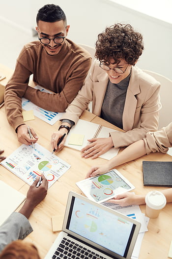 A diverse team of professionals collaborating over charts and graphs during a business meeting. HD phone wallpaper
