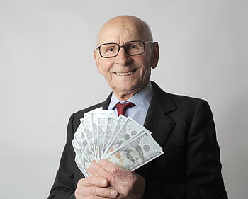 Senior man in a suit with glasses holding US dollars, symbolizing wealth and savings. HD wallpaper