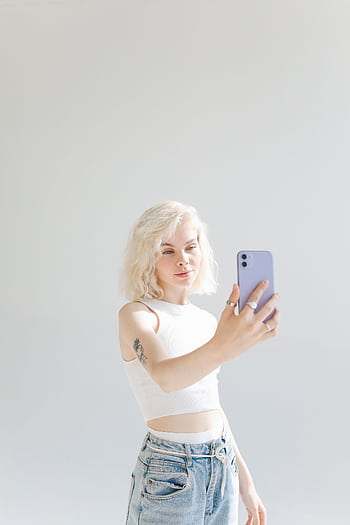 Fashionable young woman with blonde hair taking a selfie against a white background. HD phone wallpaper