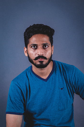 A man with facial hair in a blue shirt poses for a portrait against a gray background. HD phone wallpaper