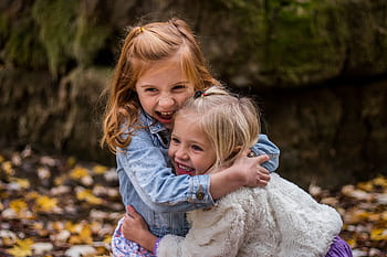Two joyful sisters hugging outdoors in autumn, surrounded by fallen leaves. HD wallpaper