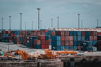 Colorful cargo containers stacked at a busy industrial port, showcasing global trade. HD wallpaper