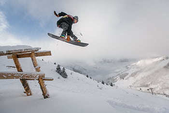 Snowboarder executing a jump over a snowy bench in a scenic winter mountain setting. HD wallpaper