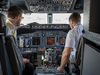 Two pilots navigating an aircraft cockpit, focused on advanced avionics and flight systems. HD wallpaper