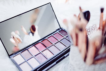 Close-up of a makeup palette and brushes reflecting in a mirror, emphasizing beauty and fashion. HD wallpaper
