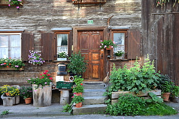 Charming rustic house entrance with wooden door and colorful flower pots creating a vibrant scene. HD wallpaper