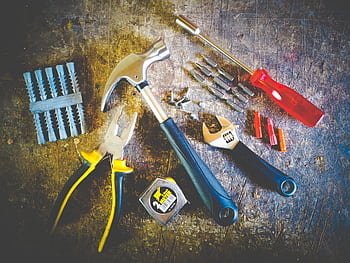Collection of hand tools including hammer, screwdriver, and pliers in a workshop setting. HD wallpaper