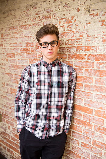 Trendy young man in glasses, plaid shirt, posing confidently against a brick wall. HD phone wallpaper