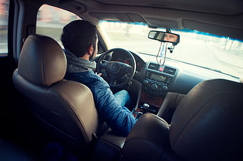 A man driving a car with focus on interior, dashboard, and steering wheel, captured from the backseat. HD wallpaper