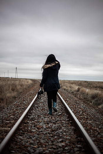 Rear view of a woman walking alone on railway tracks during twilight, conveying solitude and journey. HD phone wallpaper