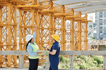 Two engineers in hardhats discuss projects at a busy construction site. HD wallpaper