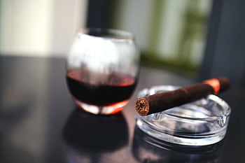 Close-up of a cigar and glass of red wine on a glass table, creating a sophisticated ambiance. HD wallpaper