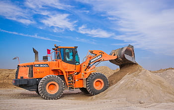 An orange bulldozer at work, moving sand under a clear blue sky on a construction site. HD wallpaper