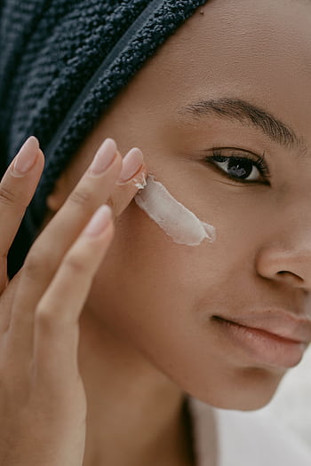 A woman gently applies moisturizing cream to her cheek, promoting healthy skin care. HD phone wallpaper