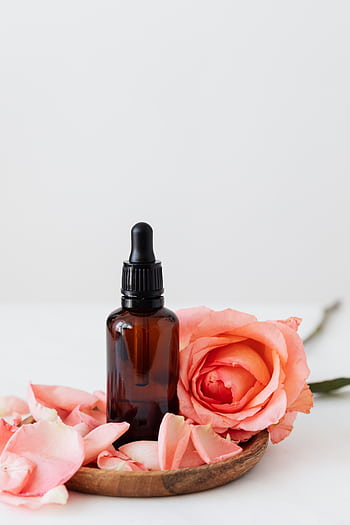 Elegant dropper bottle with pink rose petals on a wooden plate, perfect for aromatherapy or skincare. HD phone wallpaper
