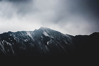 A stunning view of a snow-capped mountain peak with dramatic cloudy skies. HD wallpaper
