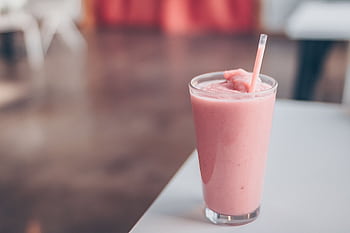 Close-up of a delicious strawberry smoothie served in a glass with a straw on a table. HD wallpaper