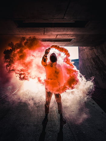 Person holding vibrant colored smoke in a dramatic urban tunnel scene. HD phone wallpaper