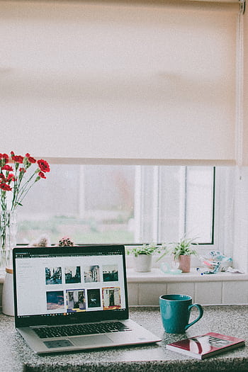 A cozy home office setup with a laptop, coffee mug, and flowers by a sunlit window, ideal for remote work. HD phone wallpaper